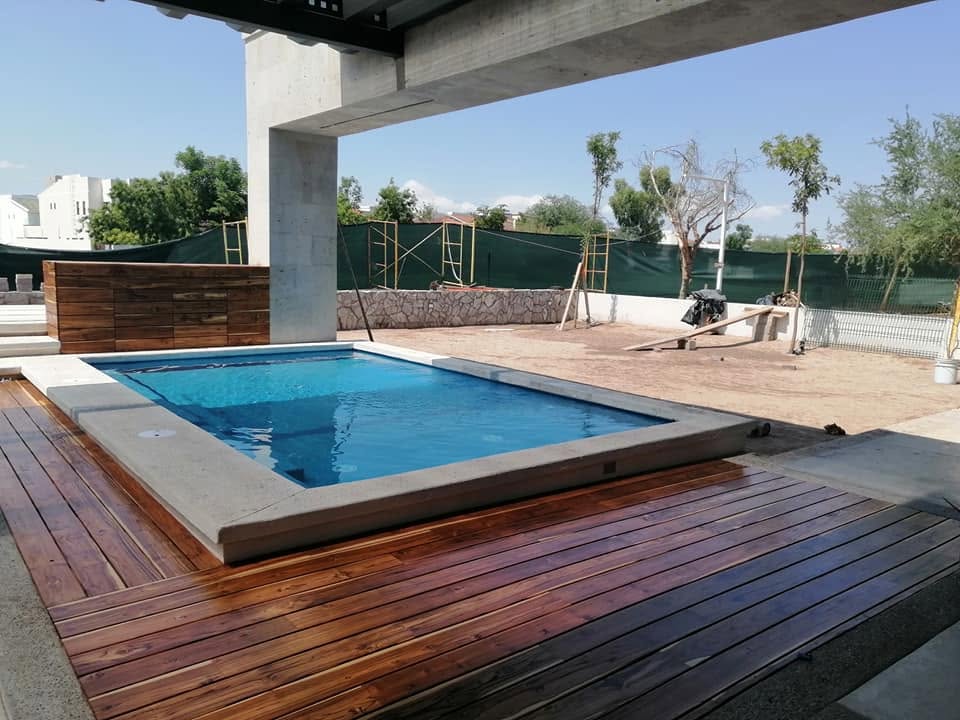Alberca con deck de madera bajo un pórtico de concreto en obra